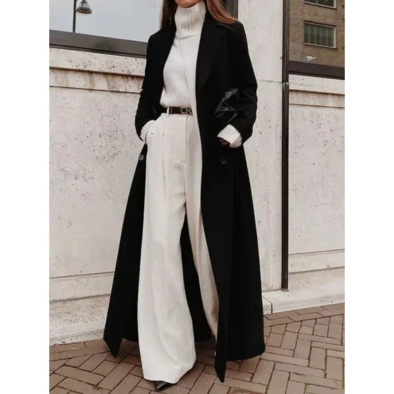 Schwarzer, bodenlanger Damenmantel mit zweireihiger Knopfleiste, breitem Revers und Taschen über weißem Outfit.