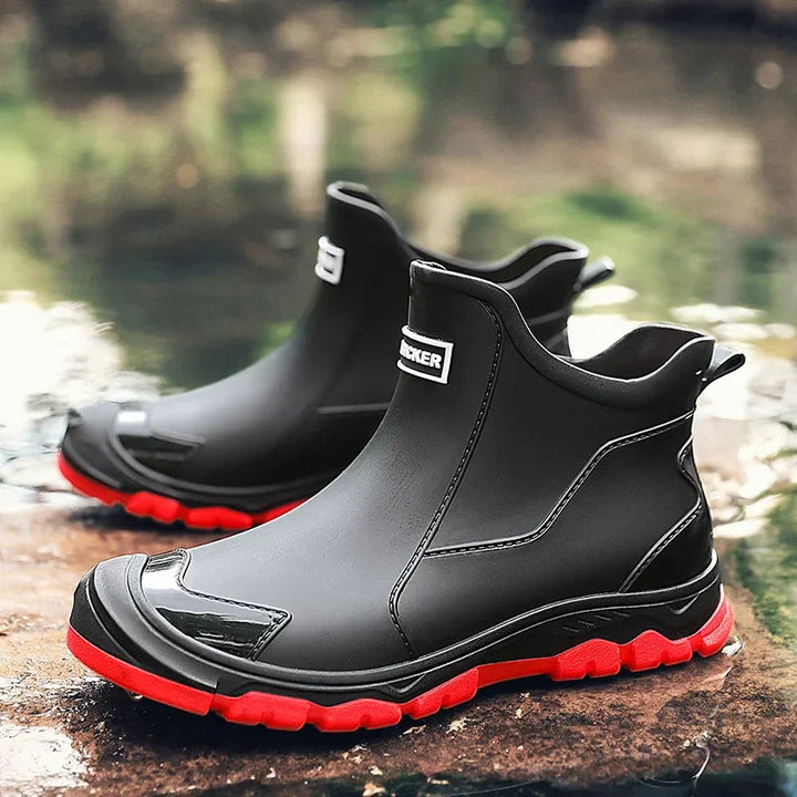 Schwarze, wasserdichte Damen-Regenstiefeletten mit roter Profilsohle und verstärkter Zehenkappe im Slip-on-Design.