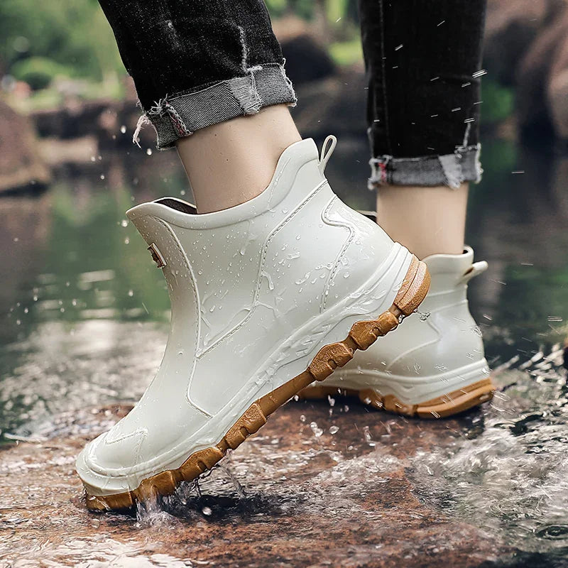 Weiße, wasserdichte Damen-Regen-Stiefeletten mit brauner Profilsohle beim Tritt in eine Pfütze.