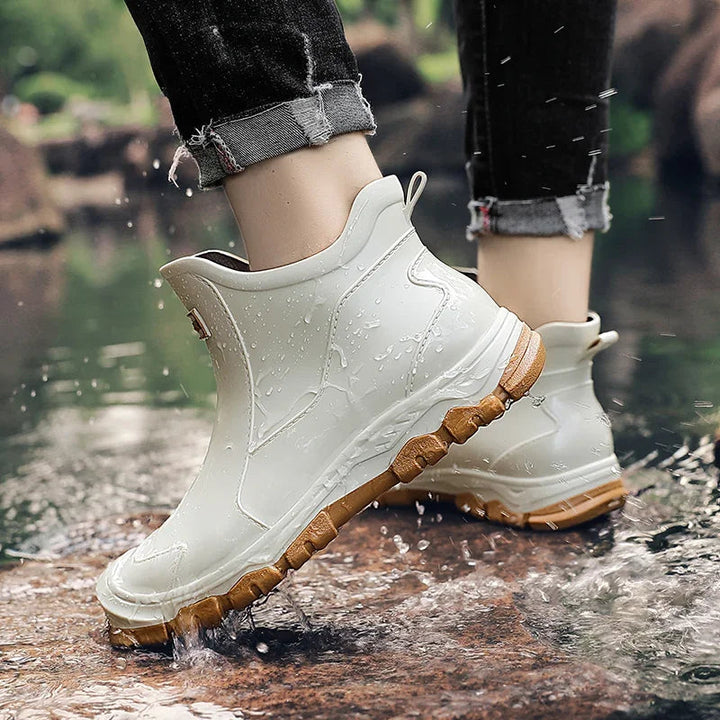 Weiße, wasserdichte Damen-Regen-Stiefeletten mit brauner Profilsohle beim Tritt in eine Pfütze.