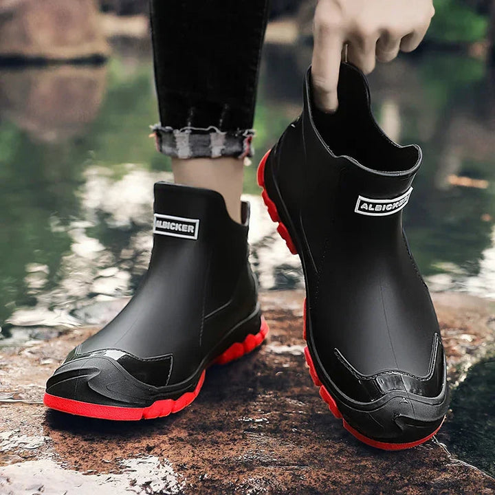Schwarze, wasserdichte Damen-Regenstiefeletten zum Hineinschlüpfen mit markanter roter Profilsohle und verstärkter Zehenkappe.