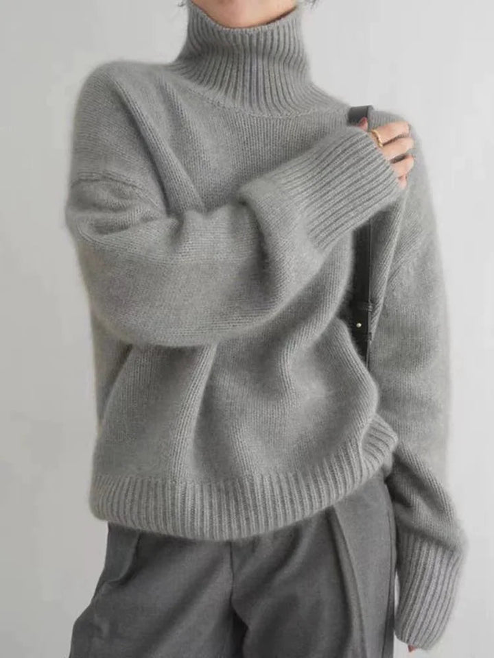 Grauer Oversized-Strickpullover mit hohem Rollkragen und gerippten Bündchen für einen modernen, gemütlichen Look.