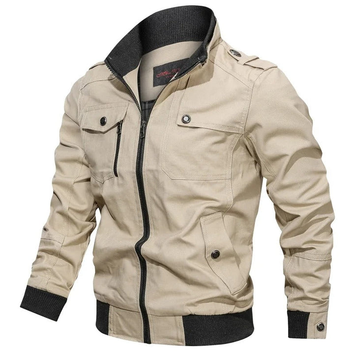 Beigefarbene Herren-Übergangsjacke im Military-Stil mit Stehkragen, Reißverschluss, Brusttaschen und schwarzen Rippbündchen.