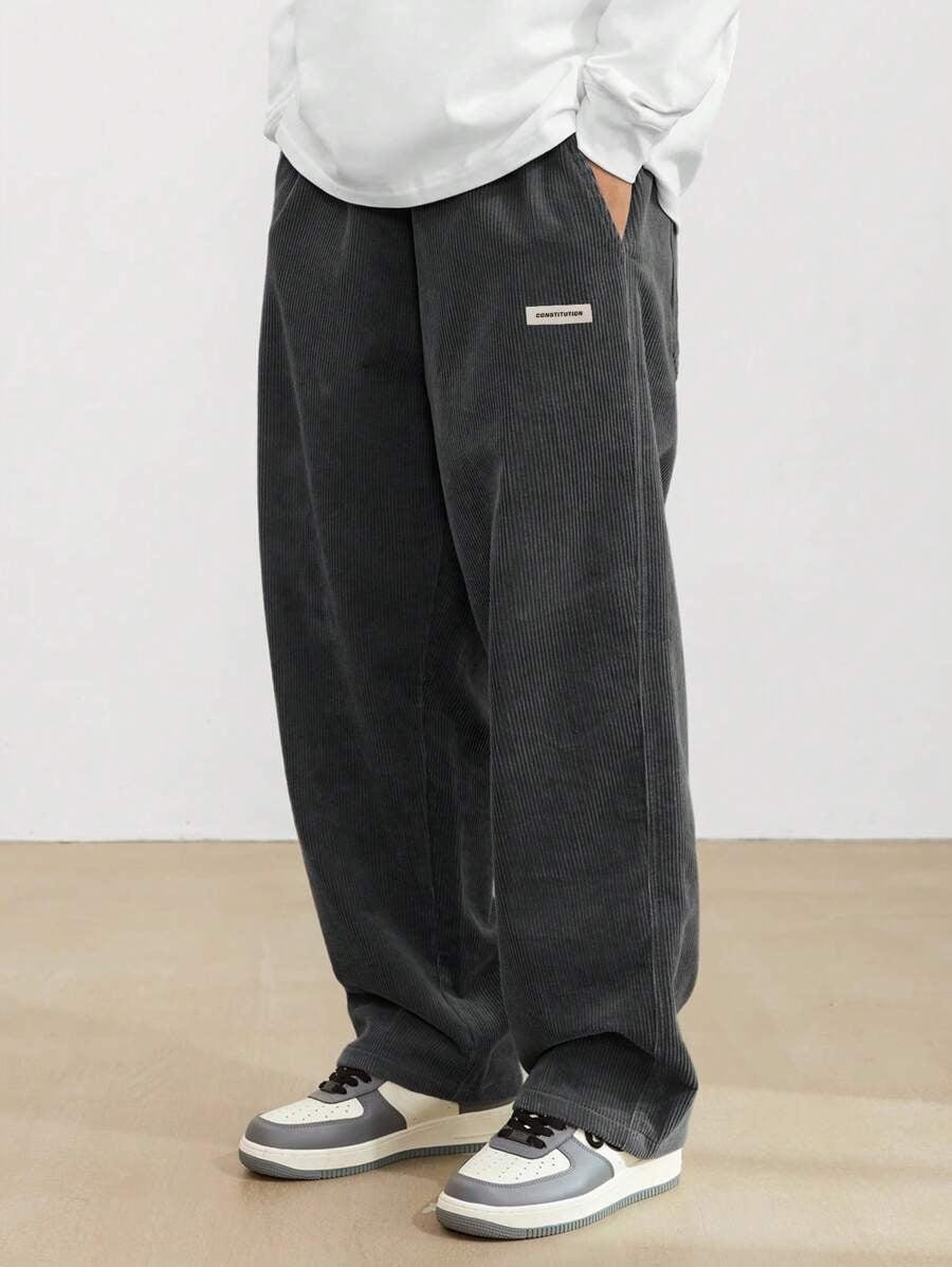 Dunkelgraue Herren-Cordhose im weiten Schnitt mit elastischem Bund und modernem Logo-Patch für lässigen Komfort.