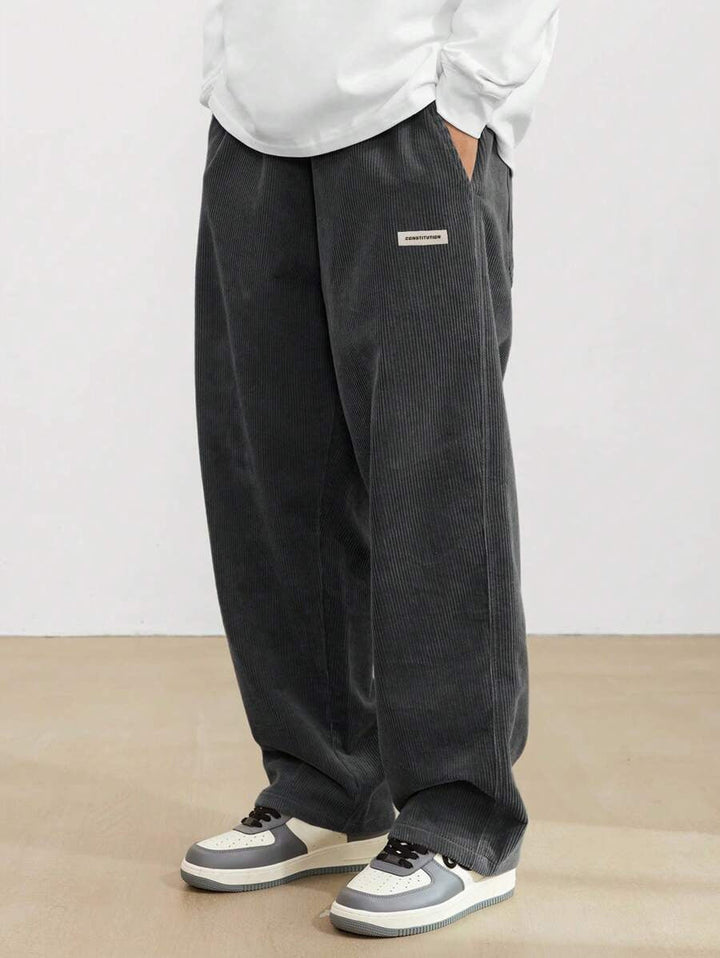 Dunkelgraue Herren-Cordhose im weiten Schnitt mit elastischem Bund und modernem Logo-Patch für lässigen Komfort.