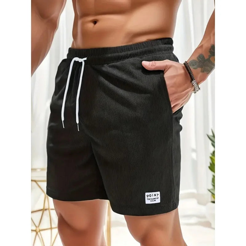 Schwarze Herren-Shorts aus geripptem Stoff mit weißem Kordelzug, elastischem Bund und kleinem Logo-Aufnäher am Saum.