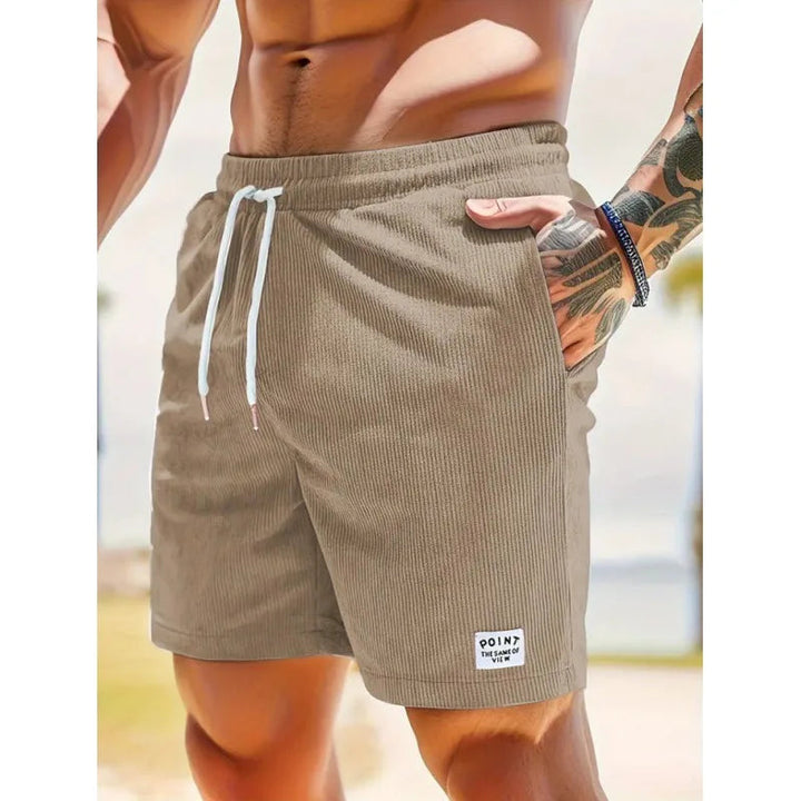 Beige Herrenshorts aus Kord mit verstellbarem weißem Kordelzug, Seitentaschen und kleinem Logo-Aufnäher am Saum.