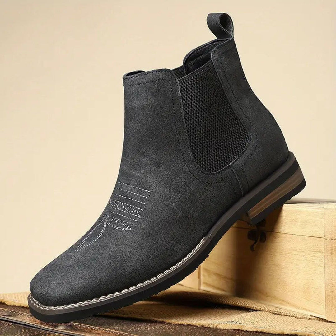 Dunkelgraue Herren-Chelsea-Boots aus Wildleder-Optik mit Western-Ziernähten, elastischen Einsätzen und Blockabsatz.