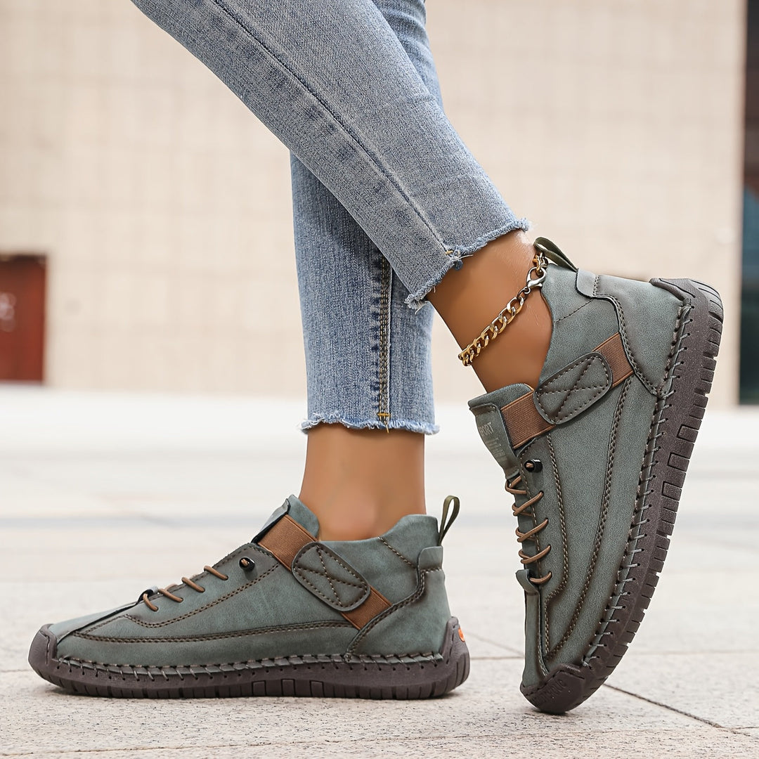 Graue Damen-Sneakers aus Leder mit Schnürung, Klettverschluss, markanten Ziernähten und flacher, profilierter Sohle.