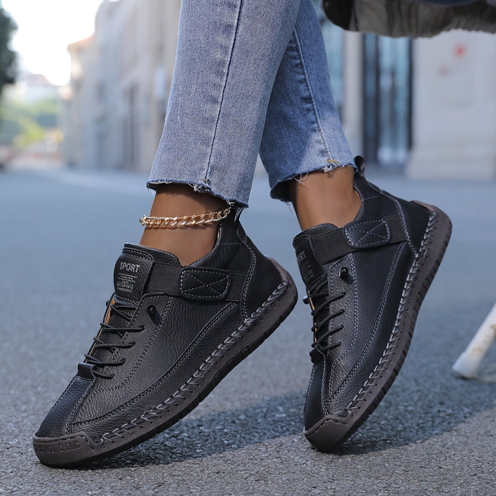 Schwarze Damen-Sneakers aus strukturiertem Leder mit Schnürung, Klettverschluss und markanten Ziernähten an der Sohle.