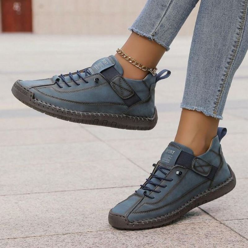 Blaue Damen-Sneaker mit Schnürung, Klettverschluss, Ziernähten und flacher Sohle an einem Fuß getragen.