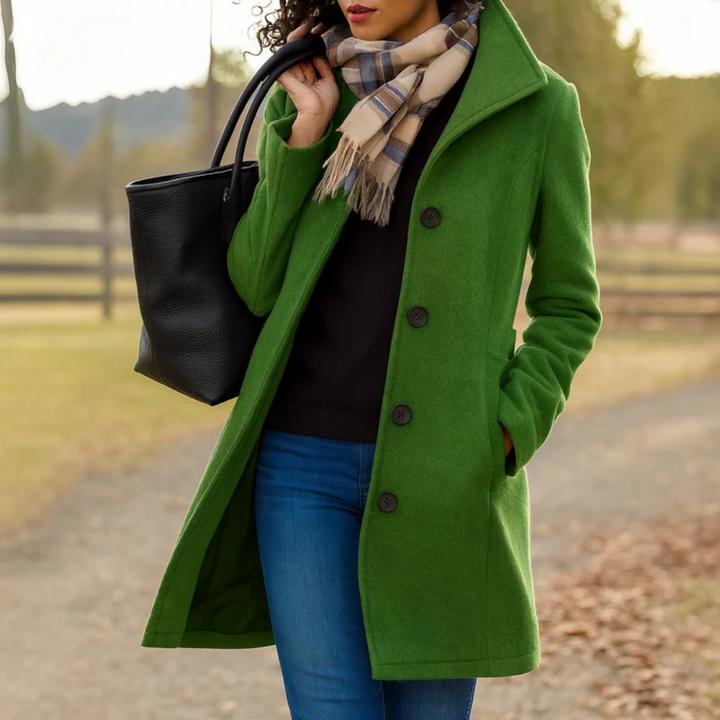 Grüner Damen-Wintermantel mit Umlegekragen, Knopfleiste und Seitentaschen, kombiniert mit schwarzer Tasche und Schal.