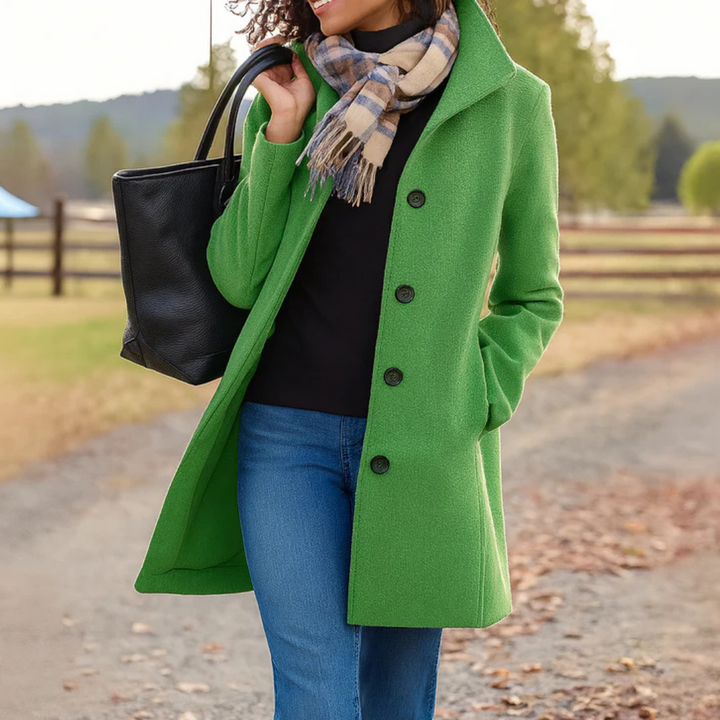 Grüner Damen-Wintermantel mit Knopfleiste, Umlegekragen und Seitentaschen, kombiniert mit schwarzer Tasche und Schal.