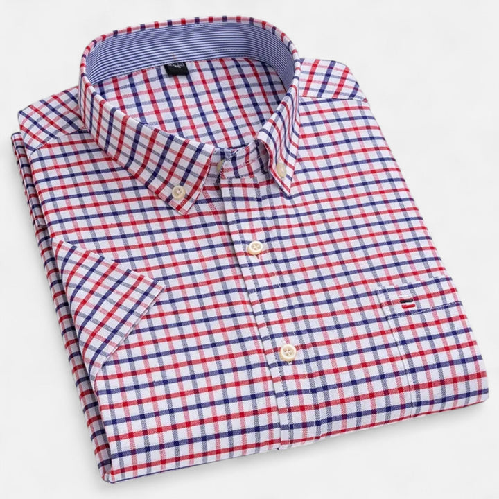 Gefaltetes Herren-Kurzarmhemd mit rot-blauem Karomuster, Button-Down-Kragen und Brusttasche auf weißem Hintergrund.