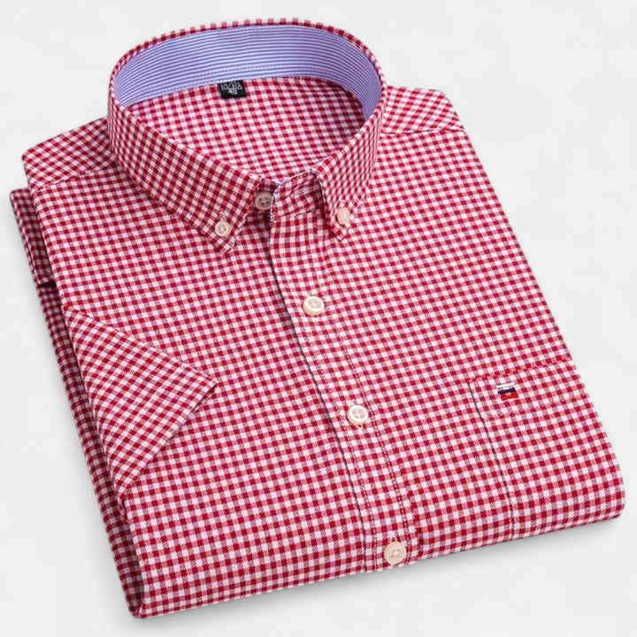 Gefaltetes Herren-Kurzarmhemd in Rot-Weiß kariert mit Button-Down-Kragen und Brusttasche auf weißem Hintergrund.